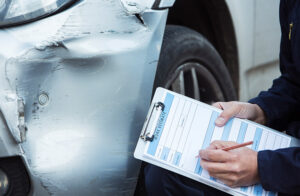 Man writing insurance claim in front of car tire